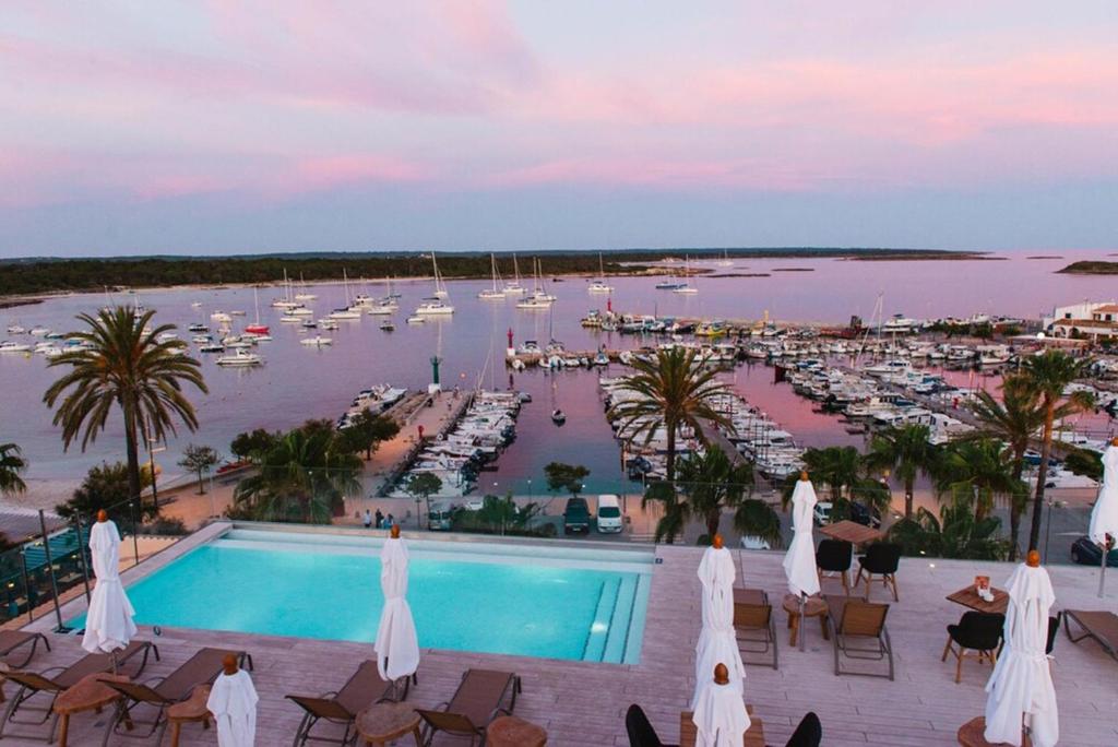 The rooftop pool of Hotel Honucai at dusk, looking out over the marina of Colònia de Sant Jordi full of moored boats, the pink and lilac sky reflected on the still water