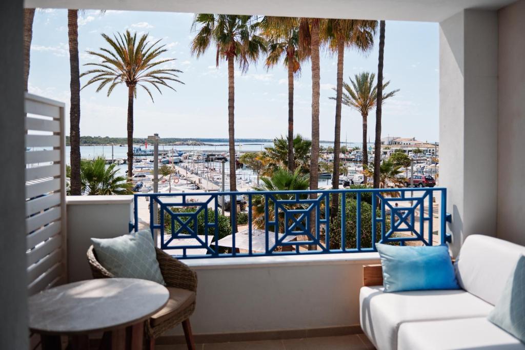 A bright Honucai room opening onto a private balcony with blue railings, palm trees and the marina beyond, a white stool and pale curtains framing the view