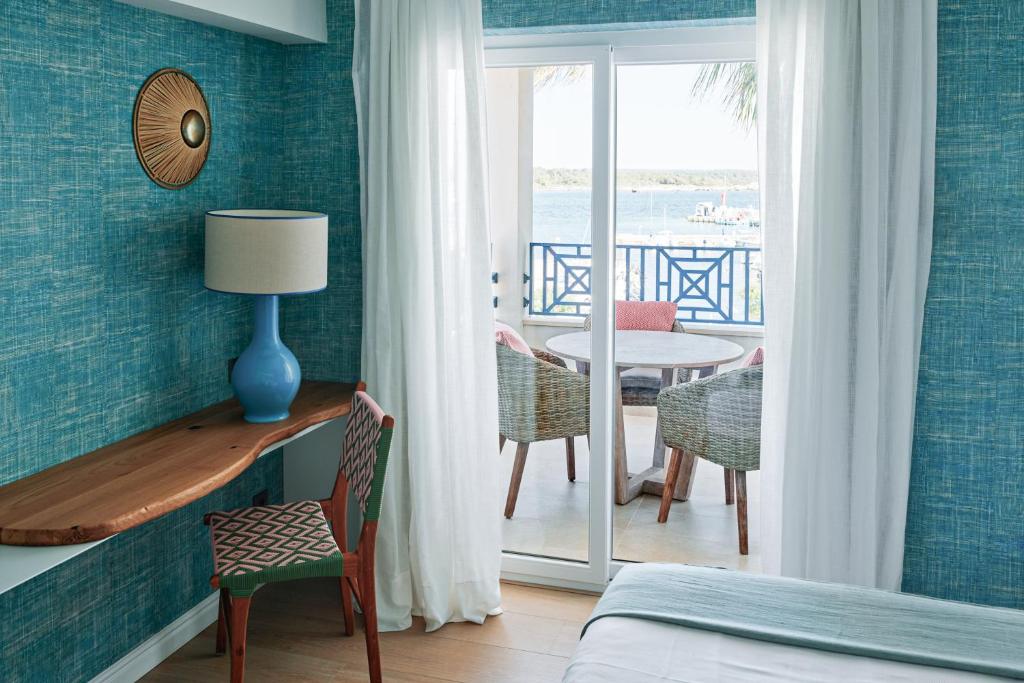 A softer green-toned Honucai room with light drapes drawn against the afternoon, an upholstered headboard and a quiet corner to sit