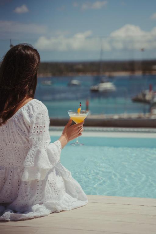 A guest in a white dress with a cocktail, the bright sea behind her